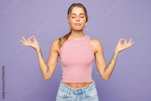 Young spiritual woman wear pink tank top casual clothes hold spreading hands in yoga om aum gesture relax meditate try to calm down isolated on plain pastel light purple background. Lifestyle concept.