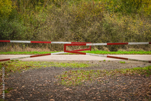 Path blocked with a red and white barrier surrounded by lush greenery in a peaceful forest area on a crisp autumn day