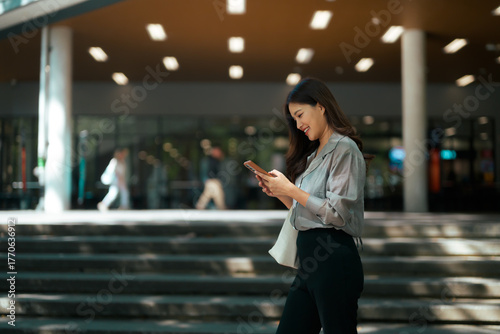 Young woman smiling, walking, using mobile phone