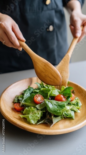 Close Up Shot of a Person Tossing Mixed Greens with Wooden Tongs. Arranging a Healthy Salad Plate in a Contemporary Kitchen. Clean Food and Mindful Eating Concept. 