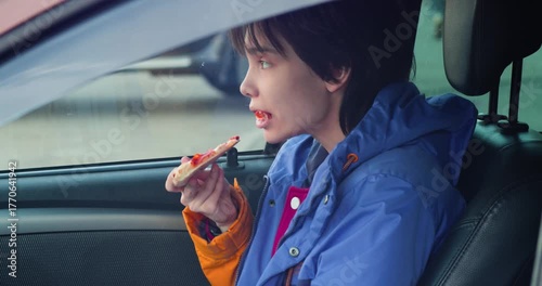 4K footage of a teenager girl eating pizza while sitting in a car. Captured joy as she devours a pizza slice, surrounded by the comforts of her car. Slow motion video.
