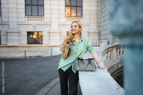 Obraz na płótnie Young woman smiling holding smartphone traveling in Vienna