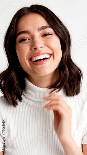 Close-up of a happy young woman with dark wavy hair smiling, wearing a white turtleneck