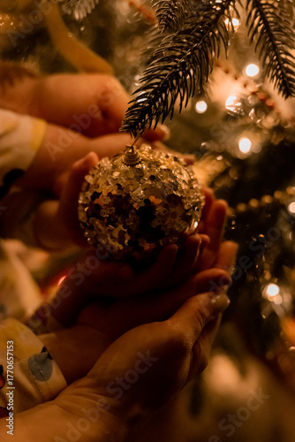 children's hands holding a Christmas tree ornament in front of a Christmas tree at night