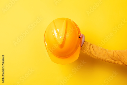 Hand holding a yellow construction helmet against a matching yellow background. Bright, minimal, and ideal for safety, construction, or industry concepts.