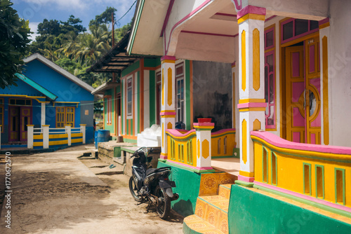 Vibrantly colored houses with a parked motorcycle under a clear blue sky. Pulau Rhun or Rhun Island, Banda, Central Maluku Regency, Indonesia