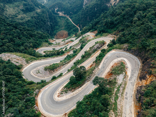 Aerial view of a winding mountain road surrounded by lush green forests and steep hills. Khau Coc Cha Mountain Pass, Bao Lac, Cao Bang, Vietnam