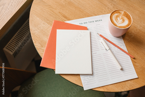 Close-up overhead view of a blank paper card, to do list, notebook, pen and pencil, cup of cappuccino on a table.