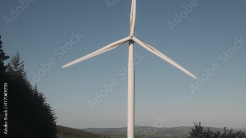 Wind turbine rotating on a sunny day in Ireland, with scenic landscape views.