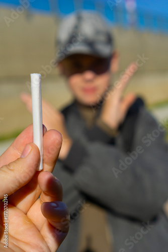 Konstfotografi Hand offering a white cigarette or rolled marijuana joint to a young man in a cap who refuses with a firm stop gesture, symbolizing youth anti-drug and anti-smoking campaign
