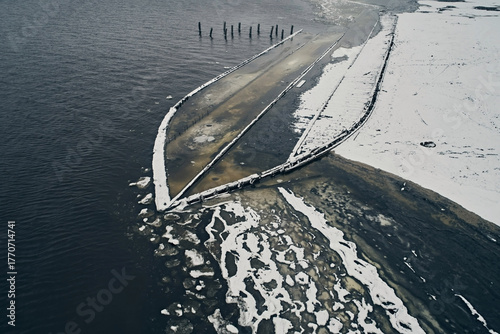 Aerial view of an abandoned wooden ship at the bottom of the river in winter against the backdrop of white snow and black water