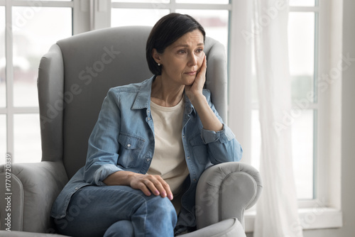 Foto Upset mid aged woman grieve in armchair suffer from menopause