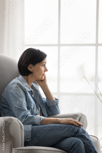 Stressed older woman sitting alone in cozy chair looking aside