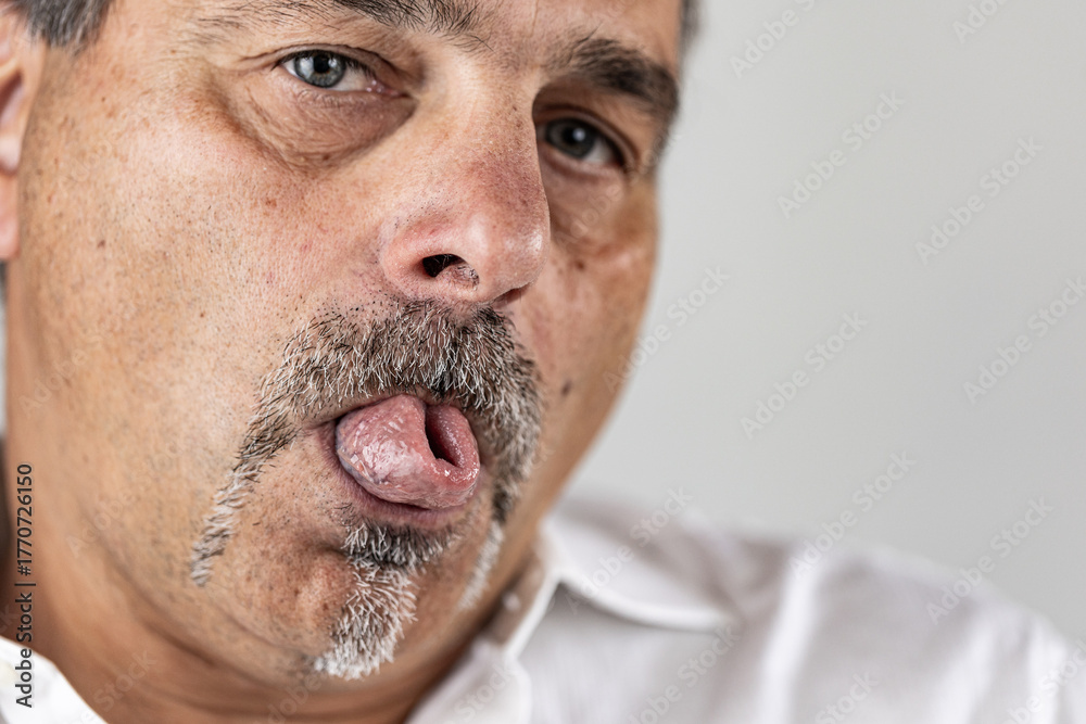 Fototapeta premium Close-up portrait of an older man making a playful facial expression while curling his tongue.