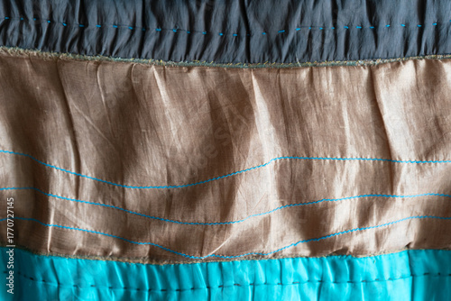 Textured fabric layers featuring vibrant turquoise, soft brown, and deep gray hues, showcasing intricate stitching patterns and rich textile details for design inspiration