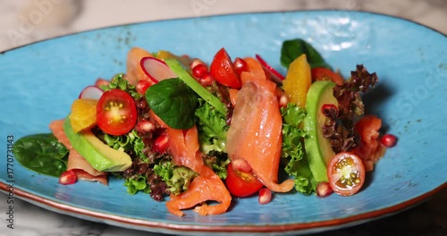Gourmet salad with smoked salmon, avocado, cherry tomatoes, radish, pomegranate, greens on turquoise plate. Healthy, fresh, colorful meal, ideal for food and diet concepts.