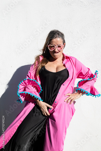 Confident Woman in Pink and Black Outfit Showing Empowerment Pose Against White Wall