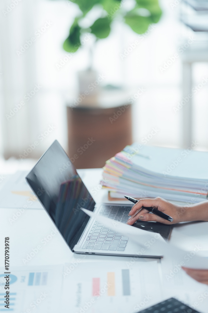 Fototapeta premium Efficiency in Focus: A person is immersed in focused work, their hand moving with purpose as they navigate a laptop's interface, with papers neatly organized beside them.