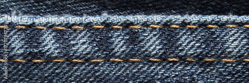 Close-up of blue denim fabric with yellow stitching detail and texture visible.