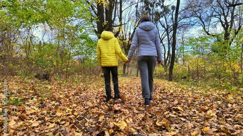 Mother walking with her son through autumn park shot from behind