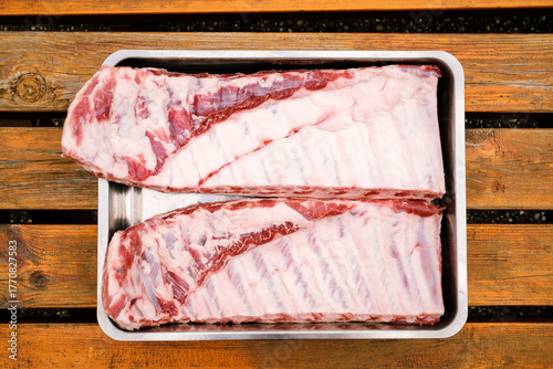 St. Louis Cut Ribs (fleischige Bauchrippen vom Schwein) in Edelstahlbräter auf Holztisch