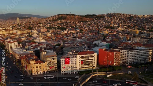 Aerial drone view of Izmir city at sunset, showing urban buildings, hills, and warm golden light over the cityscape.
