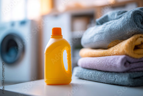 Detergent bottle standing next to stacked folded towels with a washing machine