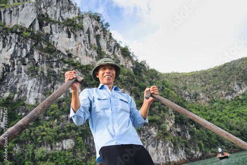 Fotografia Smiling boatman wearing a green hat and light blue shirt while rowing a tourist