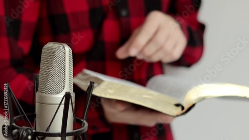 Close up of man flipping through a Bible near a microphone. Christian podcast. Preacher reads the Bible online.