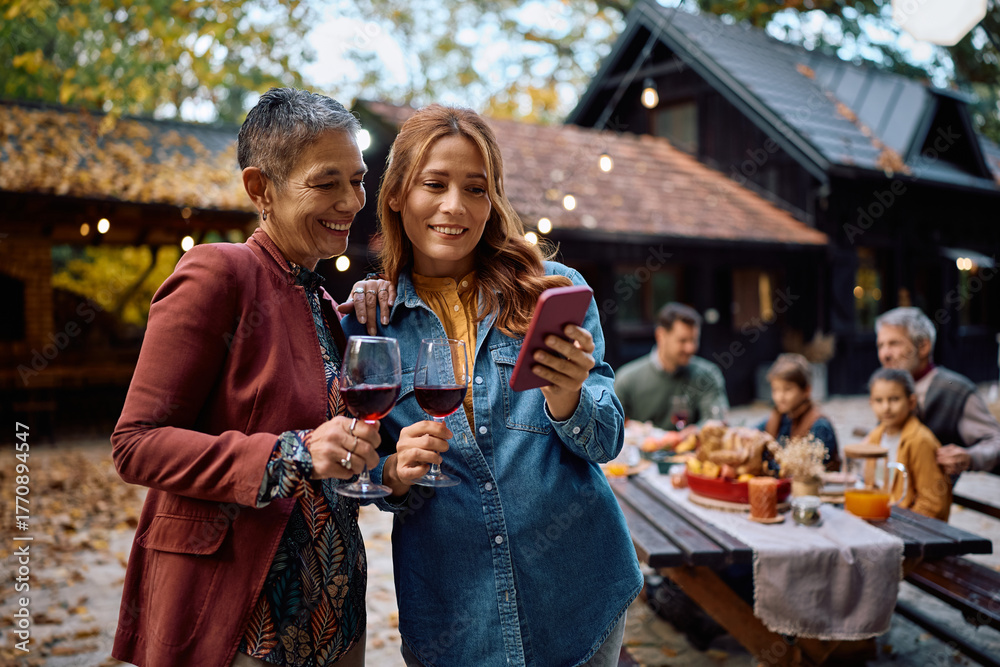 Obraz premium Happy women using cell phone during family Thanksgiving celebration.