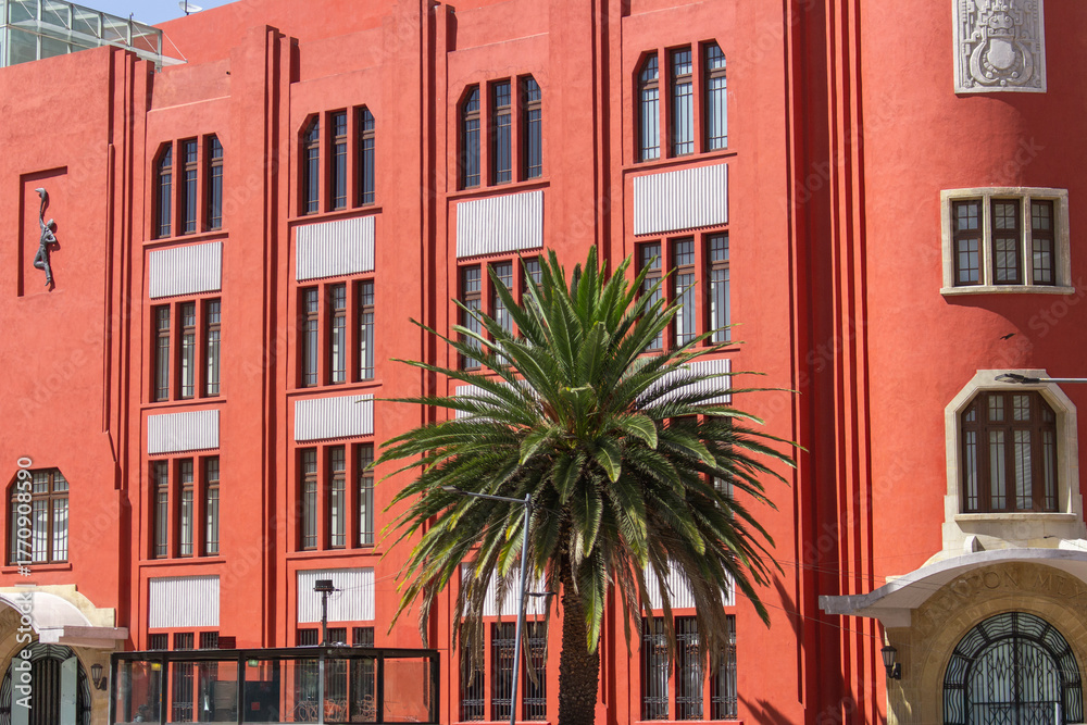 Naklejka premium Art Deco Building with Palm Trees in Mexico City – Vibrant Red Facade, Tropical Modernism, and Architectural Detail in Urban Latin American Heritage and Design Photography