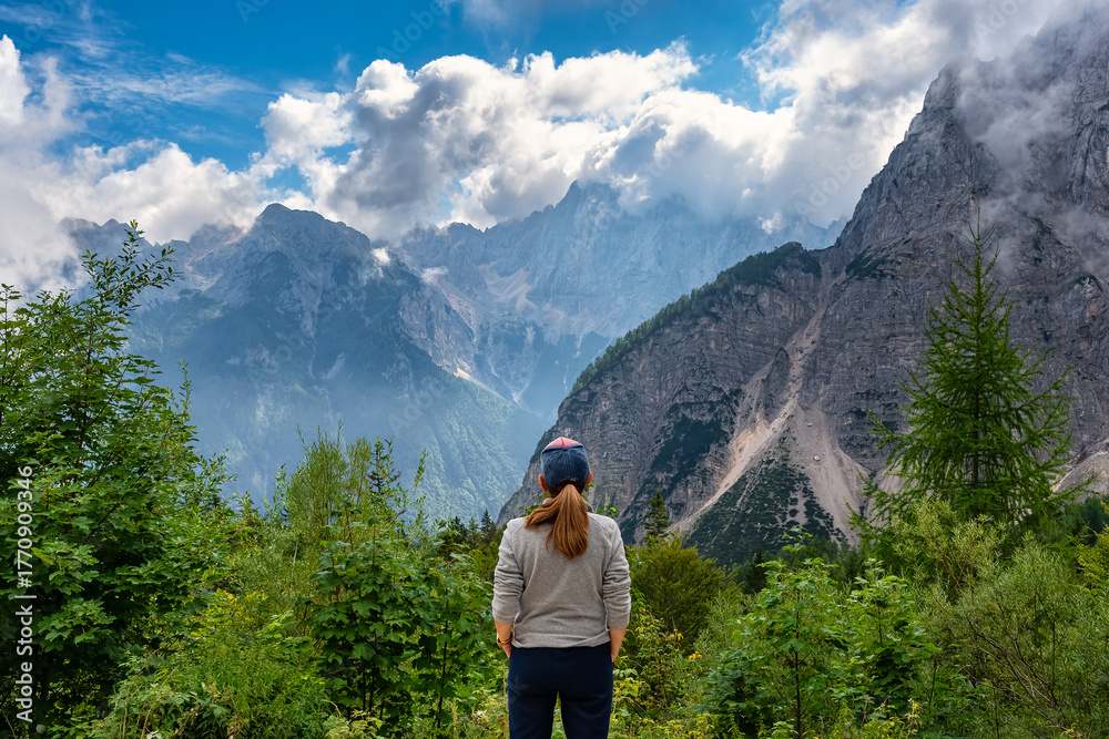 Naklejka premium Female tourist with her back gazing at the beautiful mountain scenery of the Julian Alps in Slovenia.