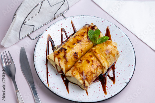 Sweet dessert: homemade egg and milk crepe with caramel, dulce de leche, cream, chocolate, and mint leaves on a china plate.