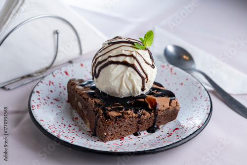 Sweet dessert: homemade brownie with ice cream on top, egg and milk with caramel, dulce de leche and cream, chocolate and mint leaf on a china plate 