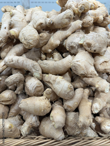 Abundant pile of fresh ginger roots with knobby, beige textures and pale skins, arranged in a rustic woven basket for a vibrant market display