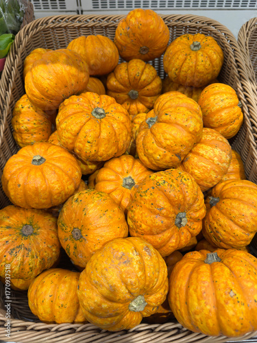 Cluster of small, vibrant orange mini pumpkins nestled in a rustic wicker basket, with textured skins evoking autumn harvest warmth and seasonal charm
