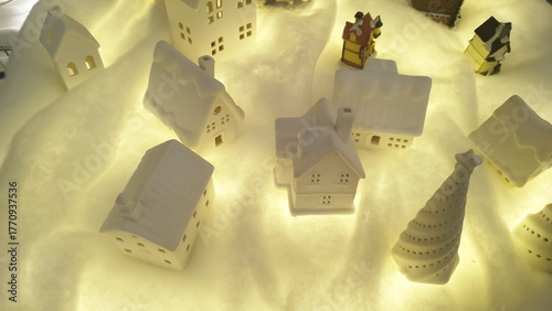 Delightful array of miniature white porcelain houses and spiral Christmas trees nestled in faux snow, illuminated with warm festive glow for a cozy holiday tableau