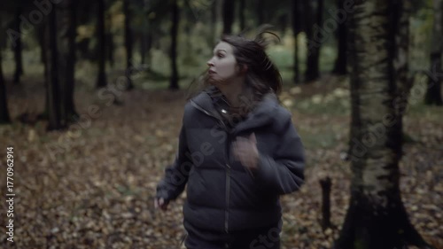 Frightened woman turning around while running in dark autumn forest