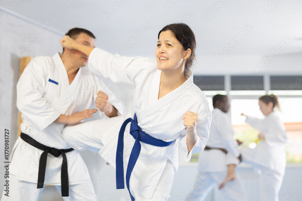 Fototapeta premium Irate middle-aged female karate practitioner fighting with her opponent in sports hall