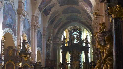 Sunlight entering through church stained glass windows. Interior view of a church featuring a golden altar, stained glass windows, and religious statues