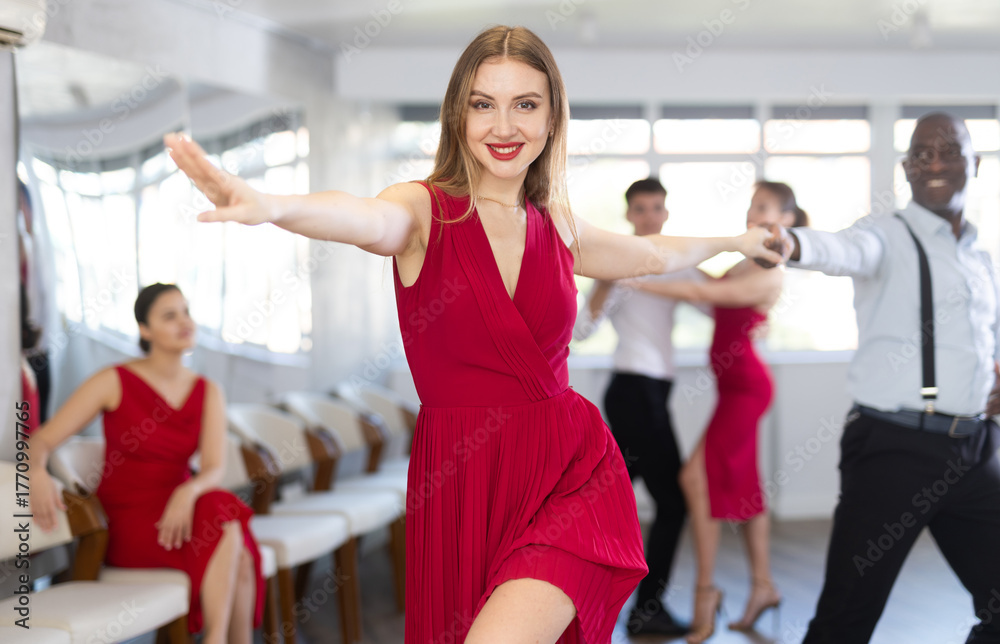 Obraz premium Positive adult woman in vibrant red dress enjoying active dances with black male partner in modern dance studio, practicing playful jitterbug moves..