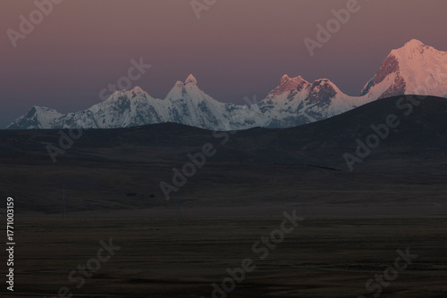 Dramatic sunset view of the Cordillera Huayhuash in Peru. The snow-capped peak of Jerupaja is prominently illuminated by golden alpenglow, rising above the shadowed mountain range.