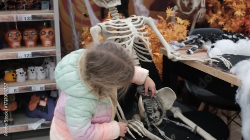 Little girl touching Halloween skeleton decoration in store