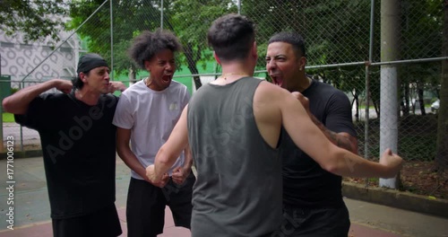 Group of Hispanic and African descent men celebrating victory on outdoor basketball court, shouting and jumping with adrenaline after scoring, energy and camaraderie