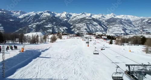 Scenic view of a ski resort with groomed slopes, ski lifts, and snow-covered mountains under a clear blue sky.