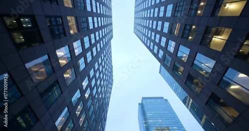 Low-angle view looking up at modern skyscrapers with numerous windows against a clear sky, emphasizing urban architecture and height.