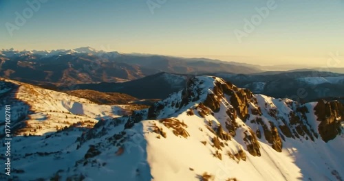 Golden hour sunlight illuminates a vast, snow-covered mountain range under a clear sky.