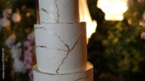 White wedding cake standing on a table outside with flower decorations