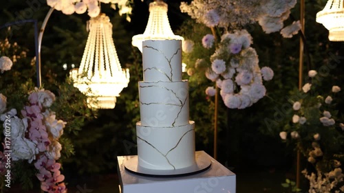 White wedding cake standing on a table outside with flower decorations