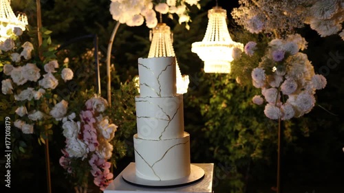 White wedding cake standing on a table outside with flower decorations